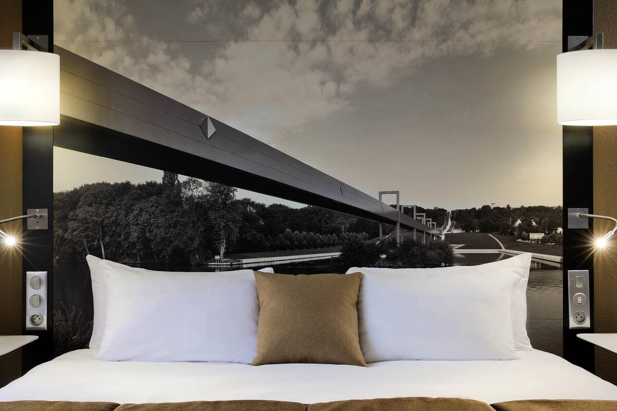 Una cama con ropa de cama blanca y marrón, vista de un puente y un cielo nocturno.