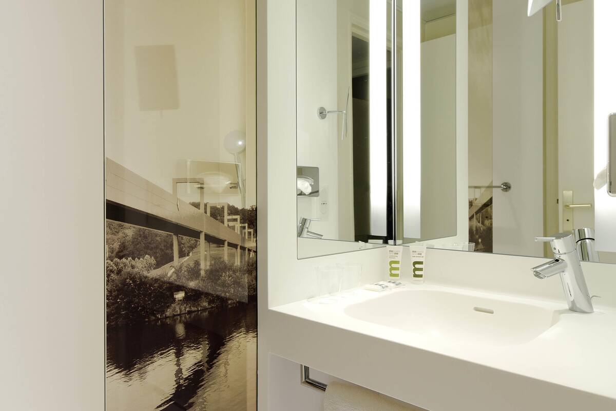 A modern bathroom with a large mirror, a white sink, and a glass partition.