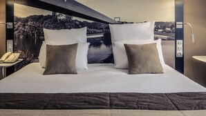 Habitación de hotel con cama, almohadas, teléfono, lámpara de pared y vistas a un lago y un puente.