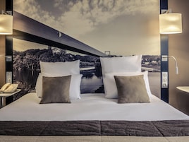 Habitación de hotel con cama, almohadas, teléfono, lámpara de pared y vistas a un lago y un puente.