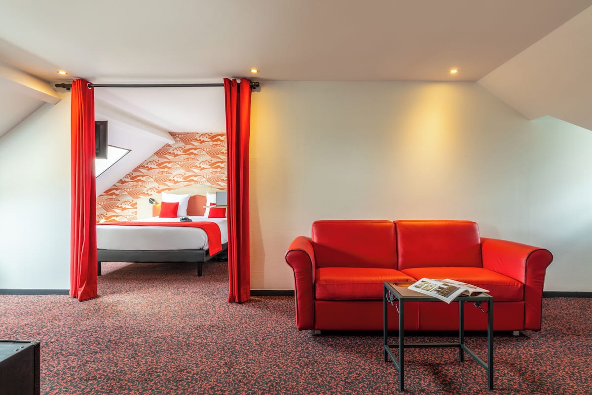 Une chambre d’hôtel avec un canapé rouge, une petite table et un lit avec une literie rouge.