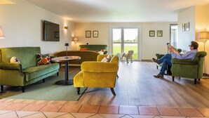 A living room with a green sofa, a yellow armchair, and a person reading a book. - ibis Styles Chartres Sud Barjouville (Barjouville)