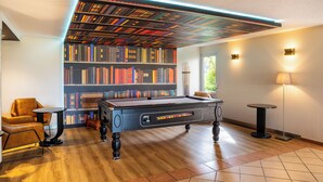A billiards table in a room with a bookshelf, a lamp, and a chair. - ibis Styles Chartres Sud Barjouville (Barjouville)