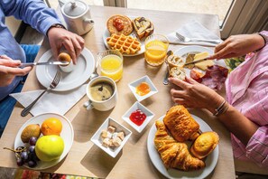 A breakfast setting with plates of food, including waffles, croissants, and fruit, and a cup of coffee.