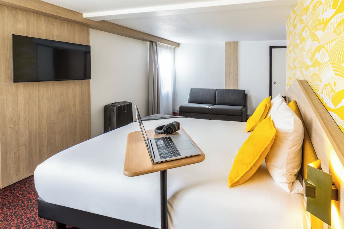 Une chambre d’hôtel moderne dotée d’un grand lit, d’un bureau avec un ordinateur portable, d’un téléviseur fixé au mur et d’un canapé.