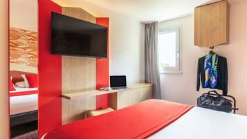 A hotel room with a bed, a desk with a laptop, a TV, and a coat rack.