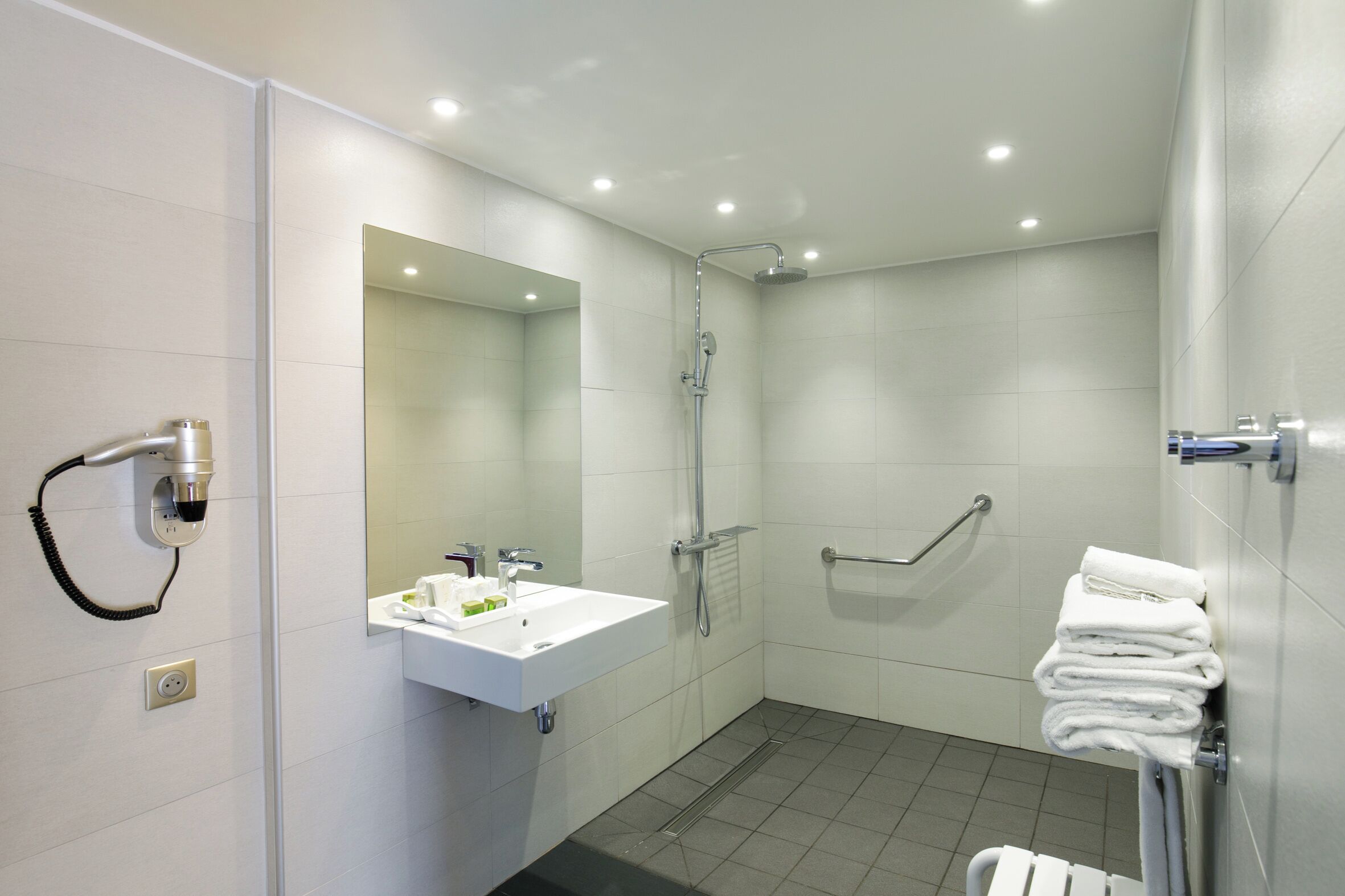 A modern bathroom with a sink, mirror, shower, and towel rack.