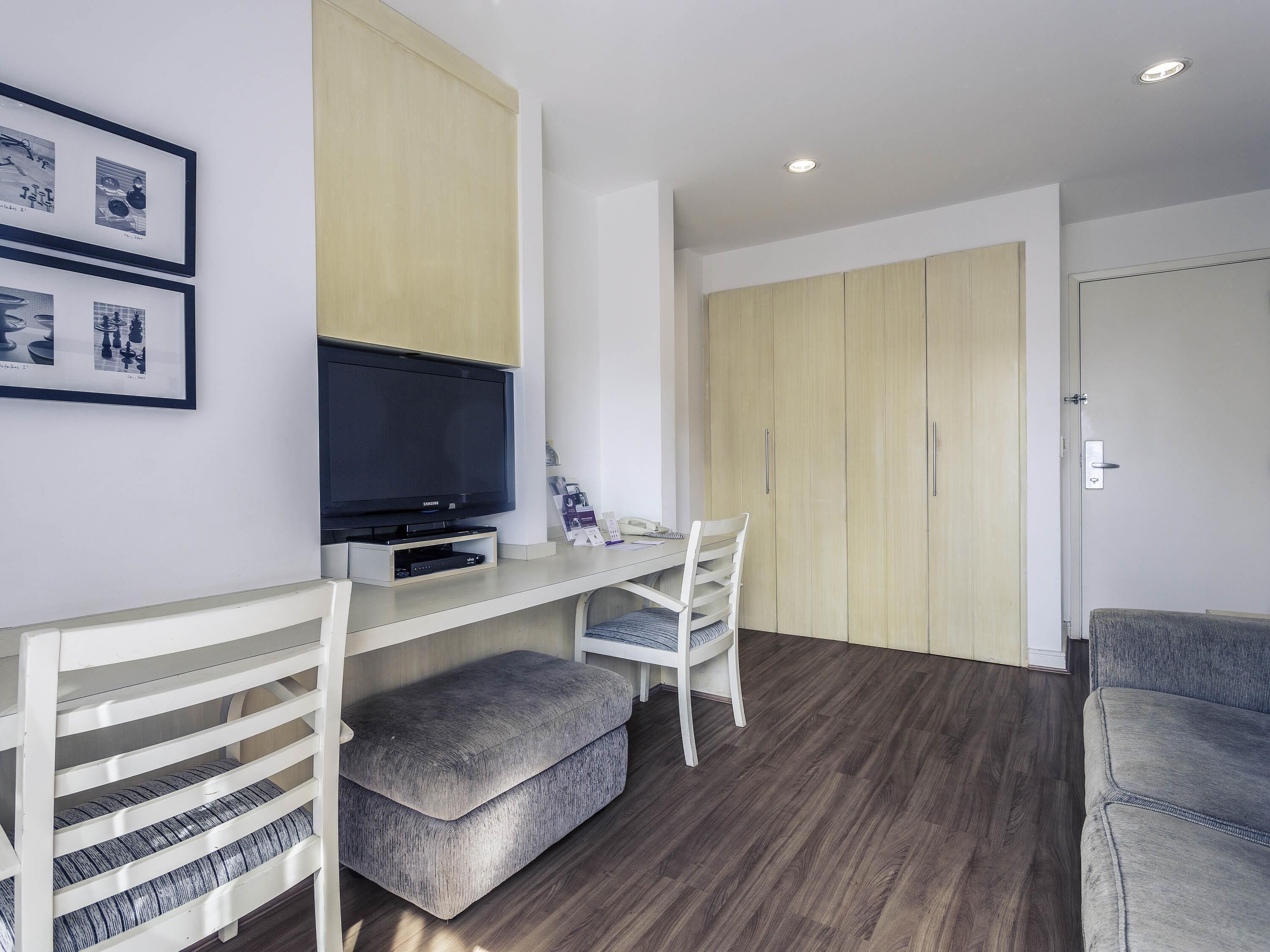 A modern room with a flat-screen TV, a desk, a chair, and a wardrobe.