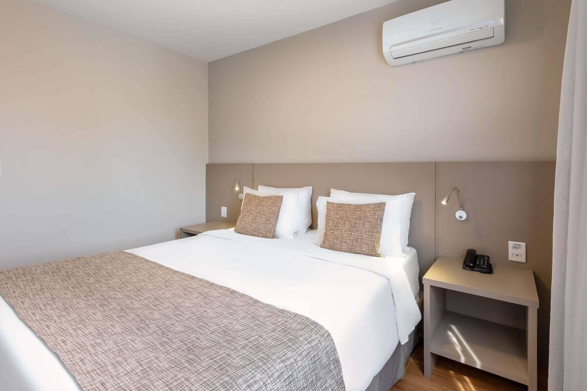Ein Hotelzimmer mit Bett, Nachttischen, einer Klimaanlage und einer Lampe.