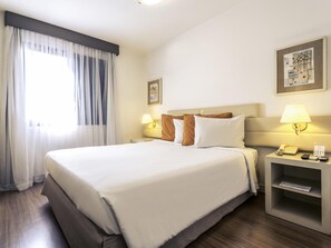 Ein Hotelzimmer mit einem großen Bett, zwei Nachttischlampen, einem Nachttisch mit Telefon und einem gerahmten Bild an der Wand.