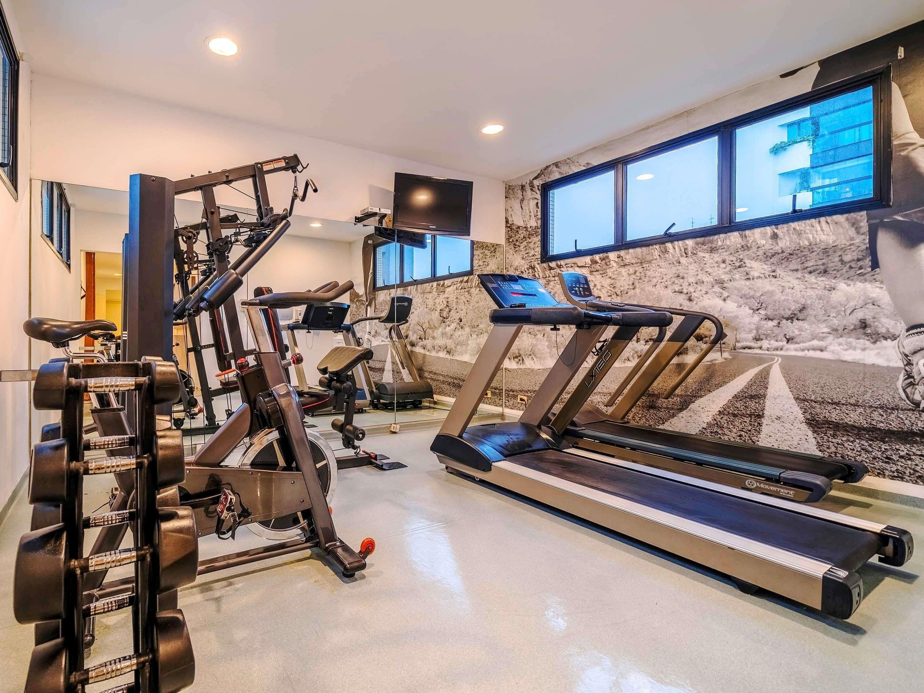 A home gym with exercise equipment, a treadmill, and a large window with a snowy landscape view.