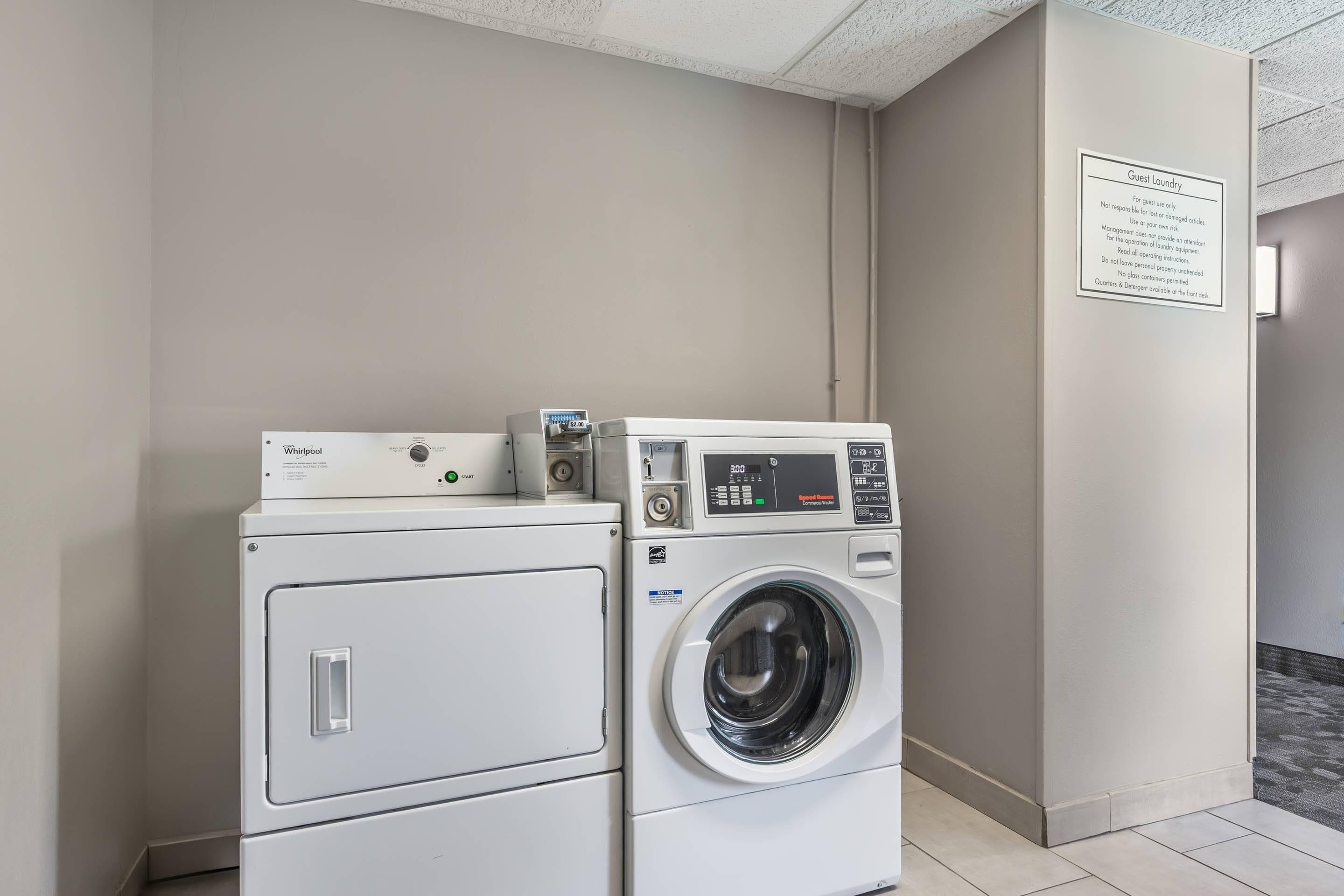 A hotel laundry room with two Whirlpool washers and dryers, a sign detailing guest laundry policies, and a tiled floor.