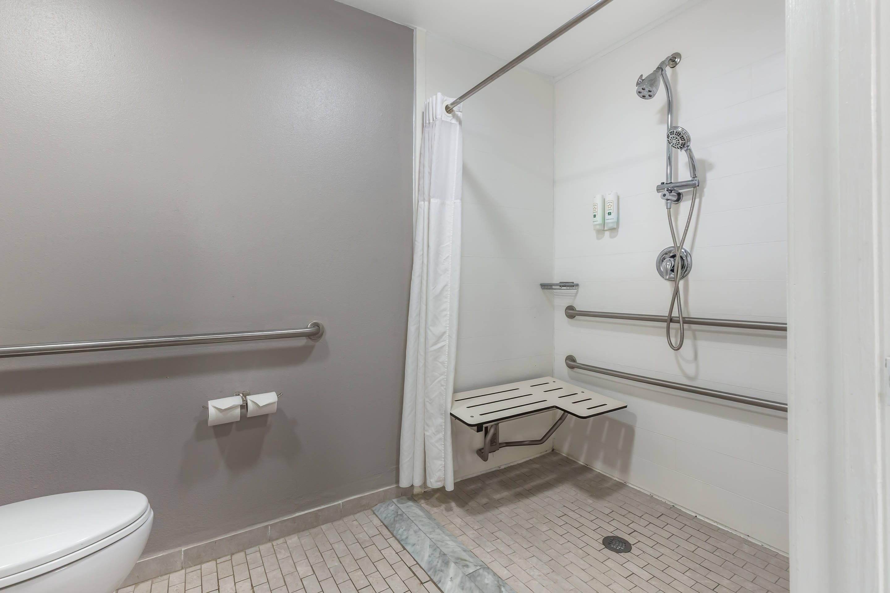 Un baño pequeño de un solo ocupante, con inodoro, ducha con cabezal de ducha manual y barra de apoyo.