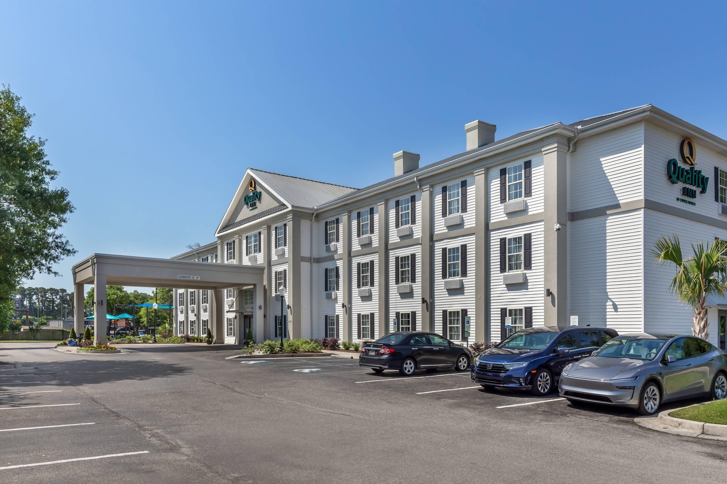 A hotel with a covered entrance, multiple parking spaces, and a clear sky.