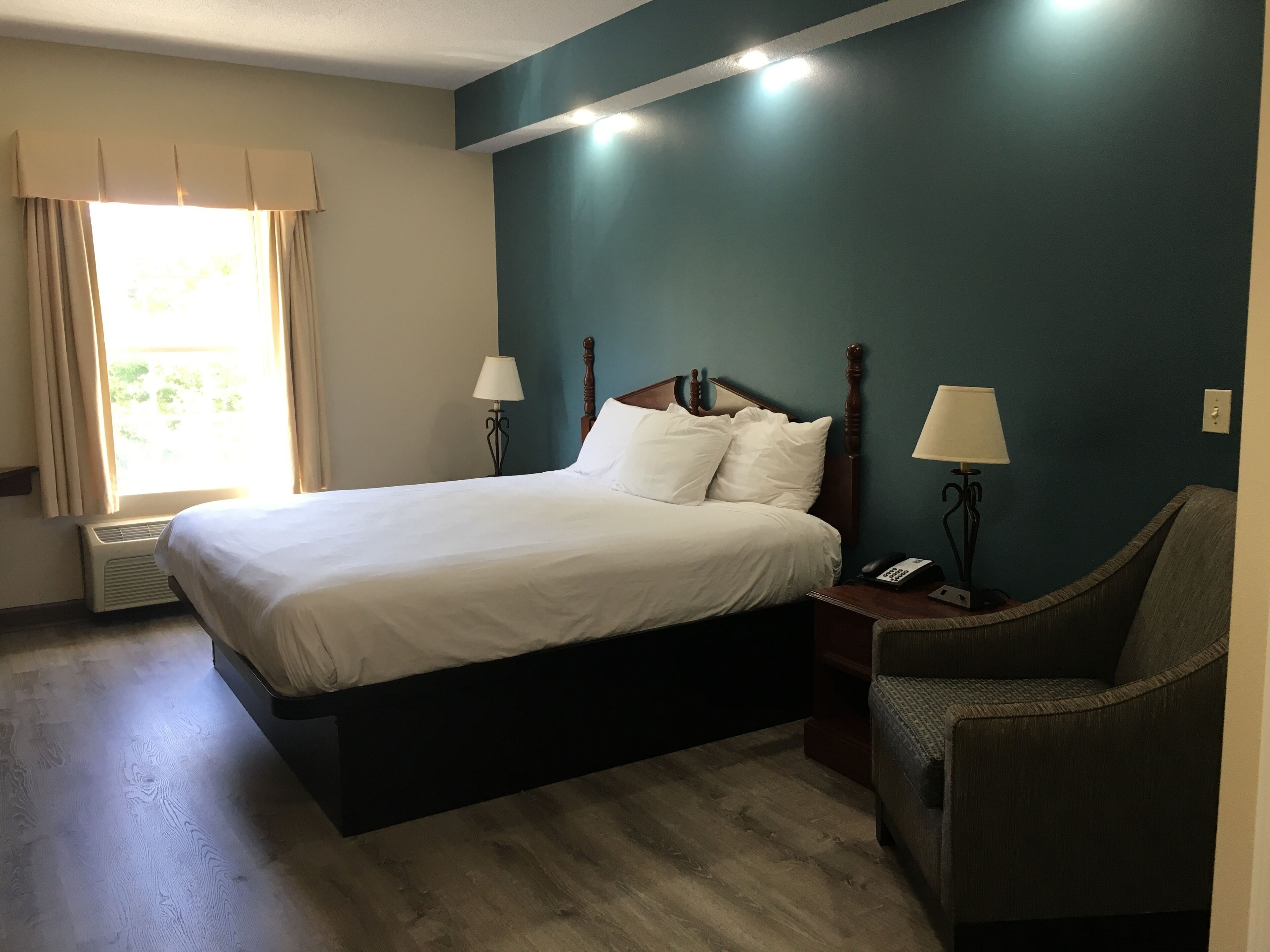 A hotel room with a large bed, two bedside tables with lamps, a chair, and a window with curtains.