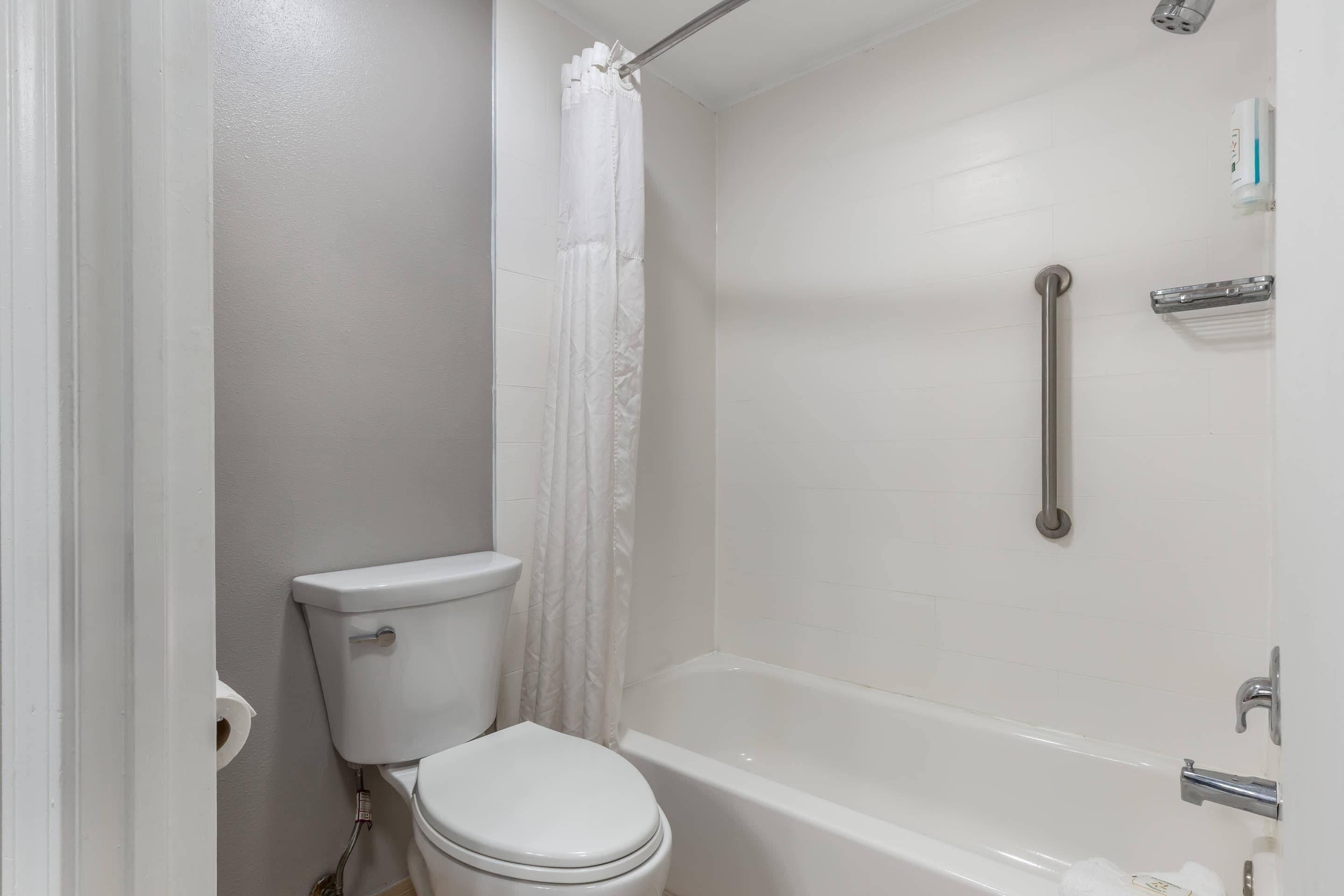 A bathroom with a toilet, a shower with a grab bar, and a bathtub.