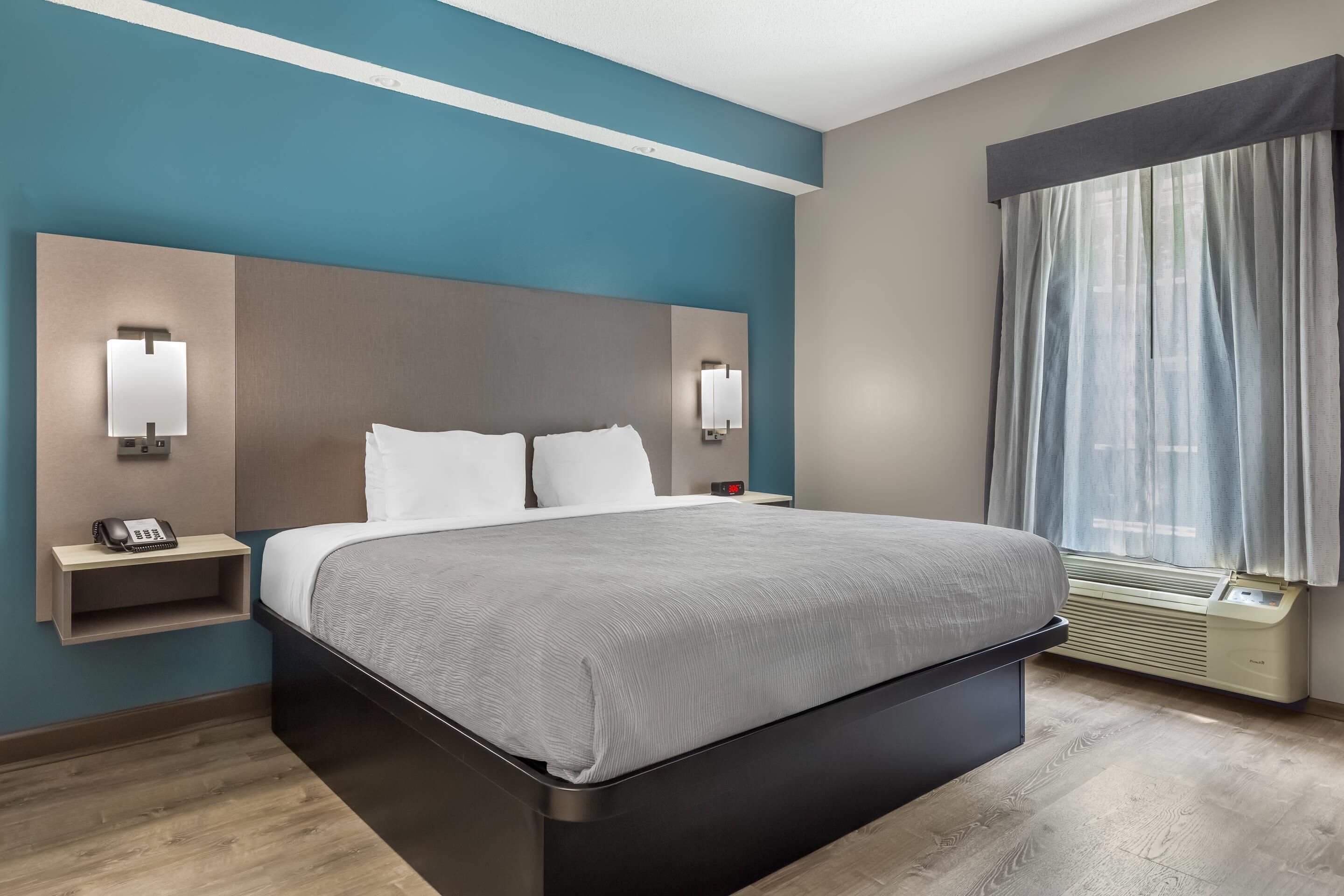 Een moderne hotelkamer met een groot bed, bedlampjes, een klein nachtkastje en een raam met gordijnen.