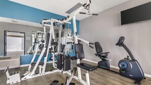 Un gimnasio con una variedad de equipos de ejercicio, incluyendo una prensa de banca, una máquina de poleas y una elíptica.