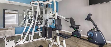 A gym with a variety of exercise equipment, including a bench press, a cable machine, and an elliptical.