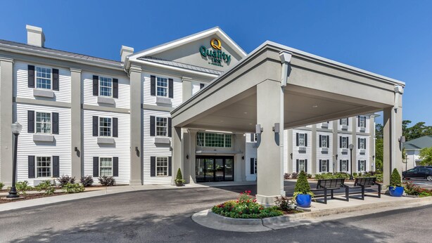 A hotel with a covered entrance, multiple windows, and a landscaped area with benches and plants.
