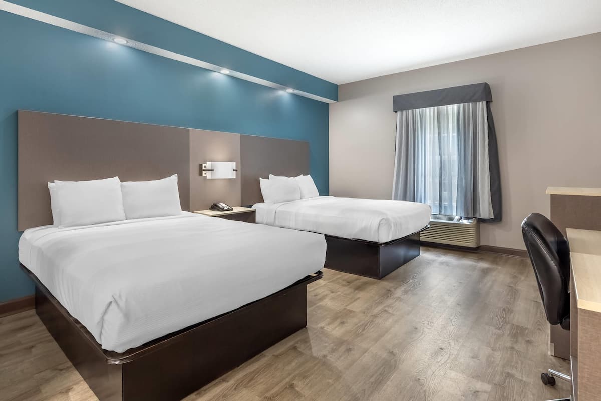 A hotel room with two beds, a desk, a chair, and a window with curtains.