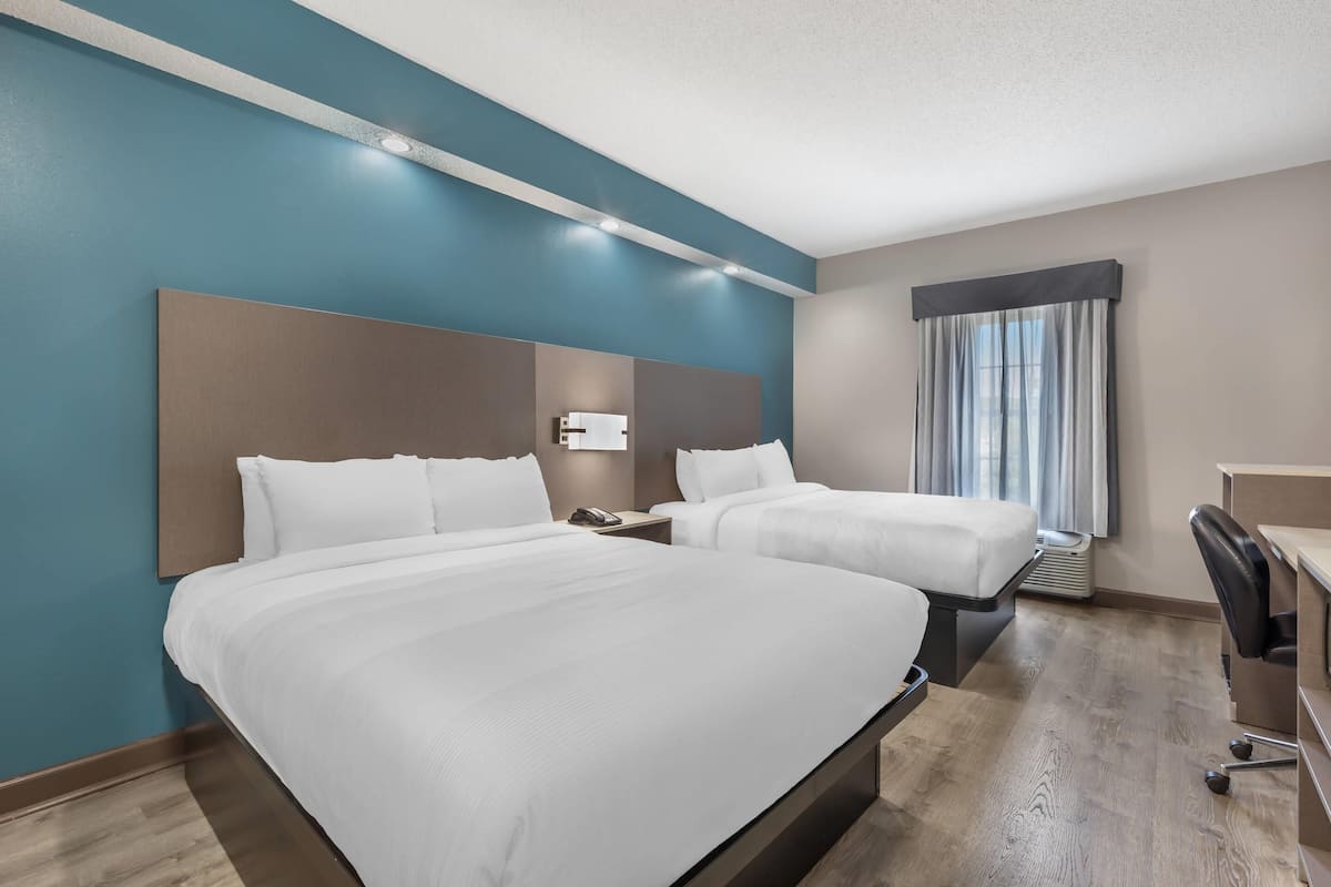 A hotel room with two beds, a desk, a chair, and a window with curtains.