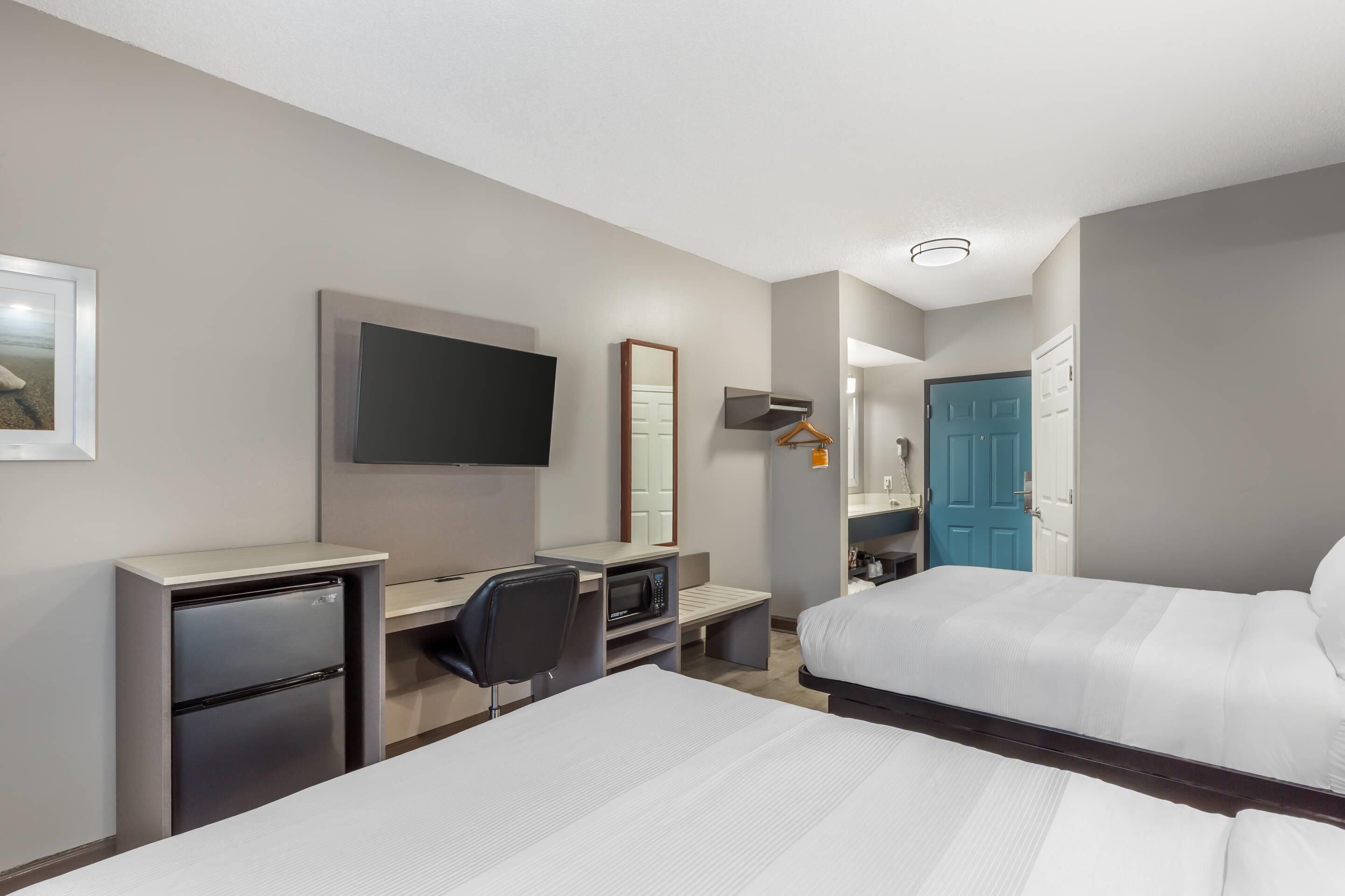 A hotel room with two beds, a desk with a chair, a microwave, a refrigerator, a TV, and a wardrobe.
