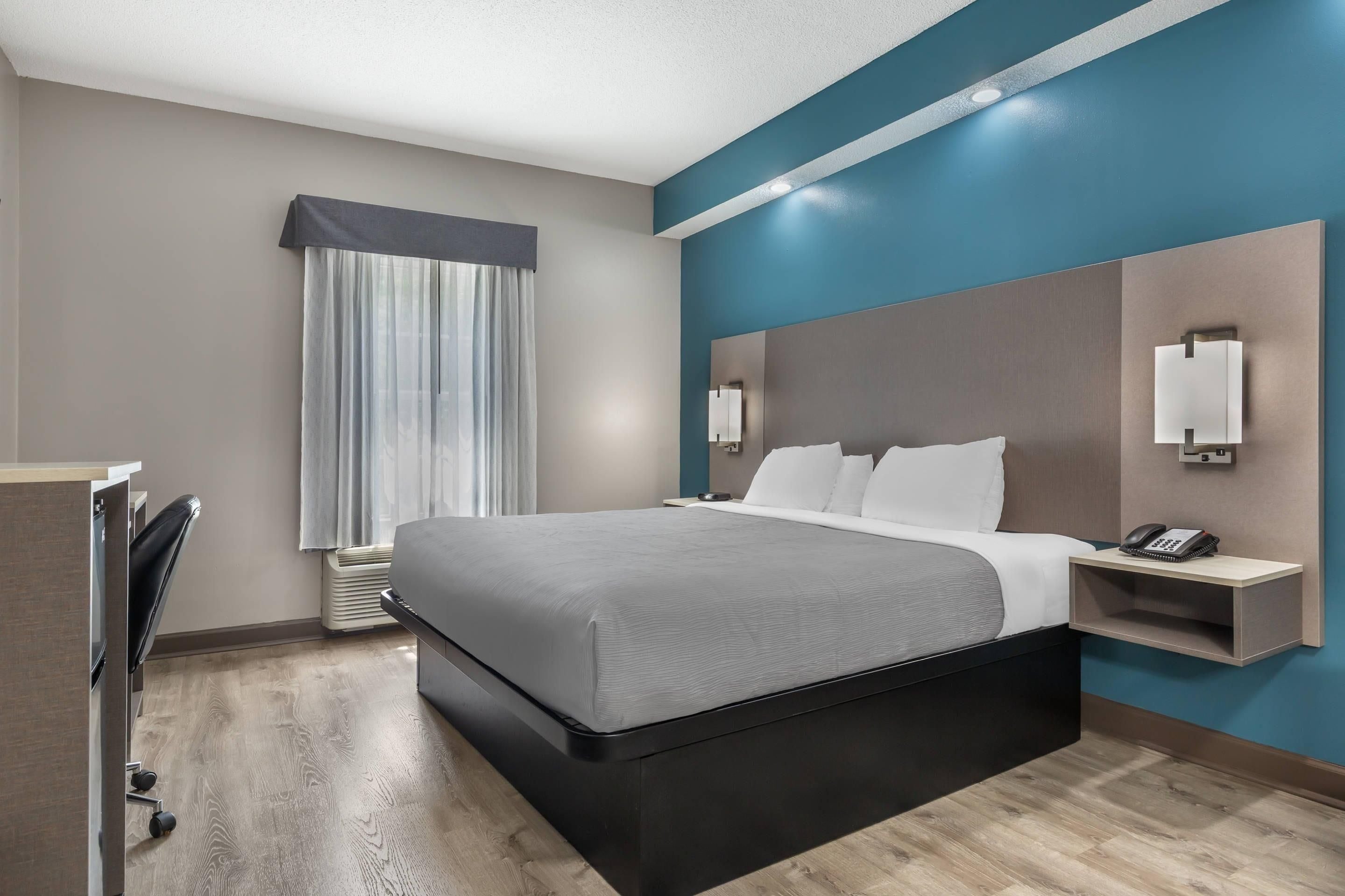 A hotel room with a large bed, a desk, a telephone, and a window with curtains.