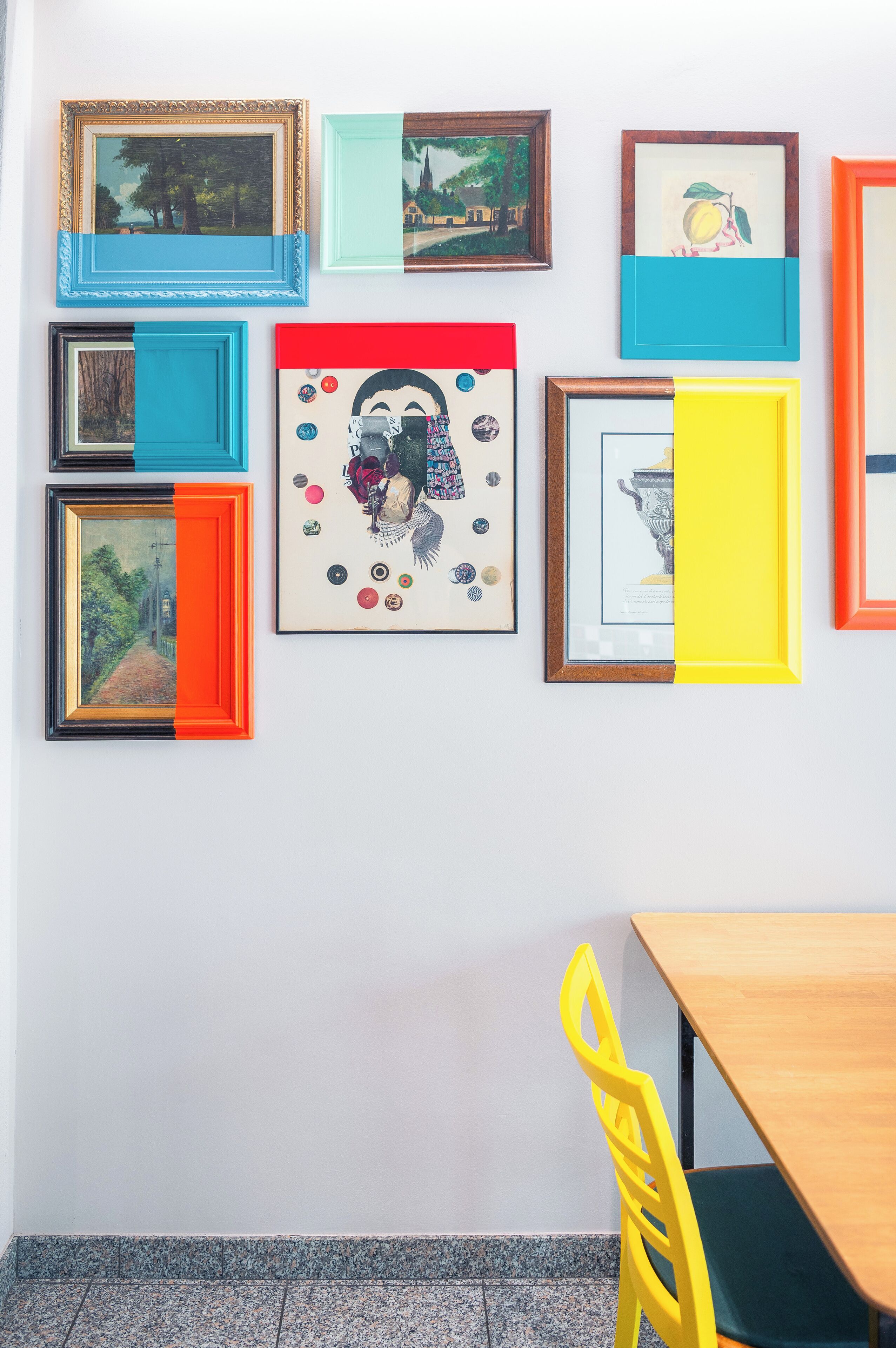 A wall with various framed artworks and a wooden table with a yellow chair.