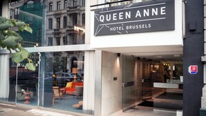 The exterior of the Queen Anne Hotel in Brussels, featuring a modern glass facade, a prominent sign, and a glimpse of the interior seating area. - Queen Anne Hotel (Brussels)