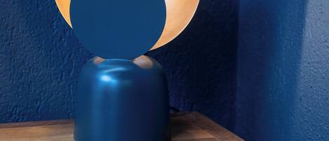 A table lamp with a blue base and a circular shade, placed on a wooden nightstand with a drawer.
