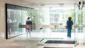 A modern lobby with a glass entrance, a reception desk, and a visible outdoor area with greenery. - Queen Anne Hotel (Brussels)
