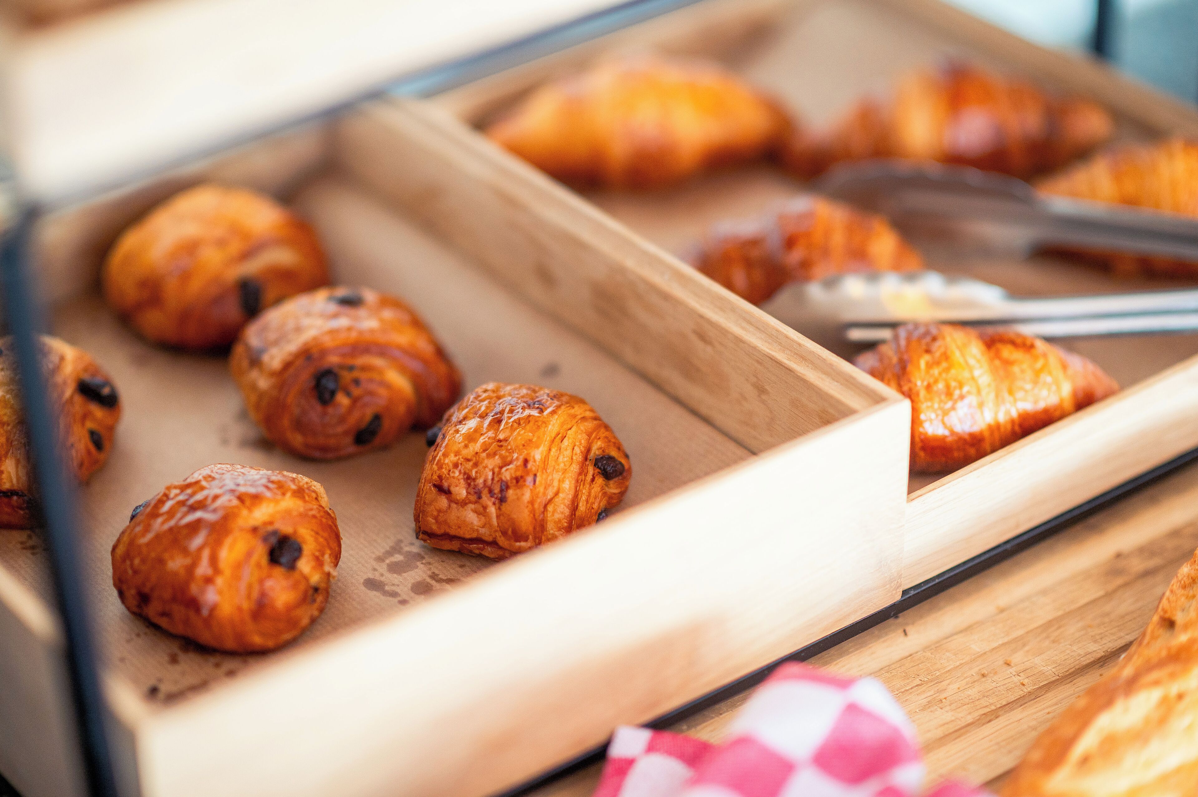 Ein Holztablett mit verschiedenen Backwaren, darunter Croissants und ein Baguette, auf einem Tisch.
