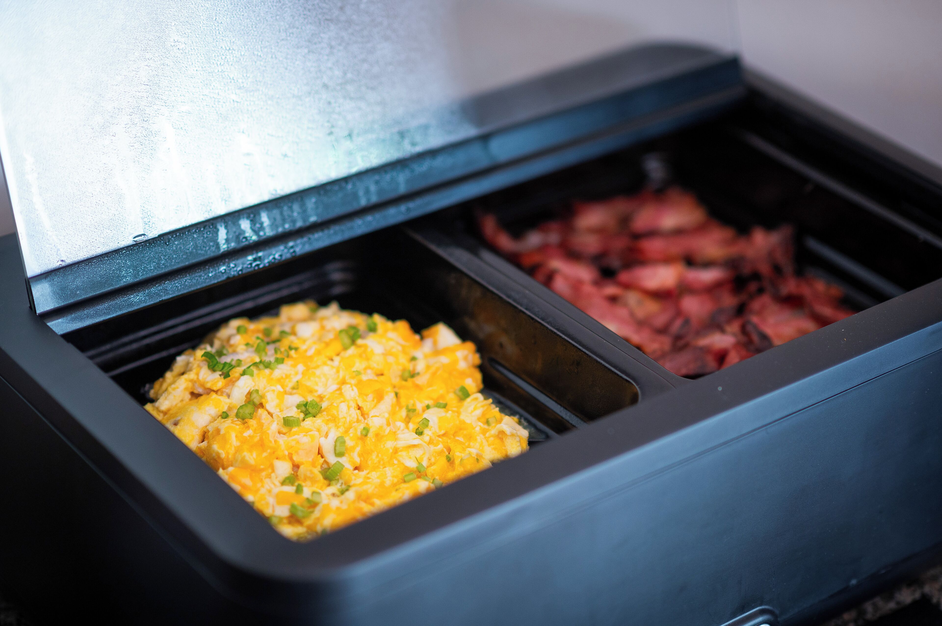 A buffet with scrambled eggs and sliced meat.