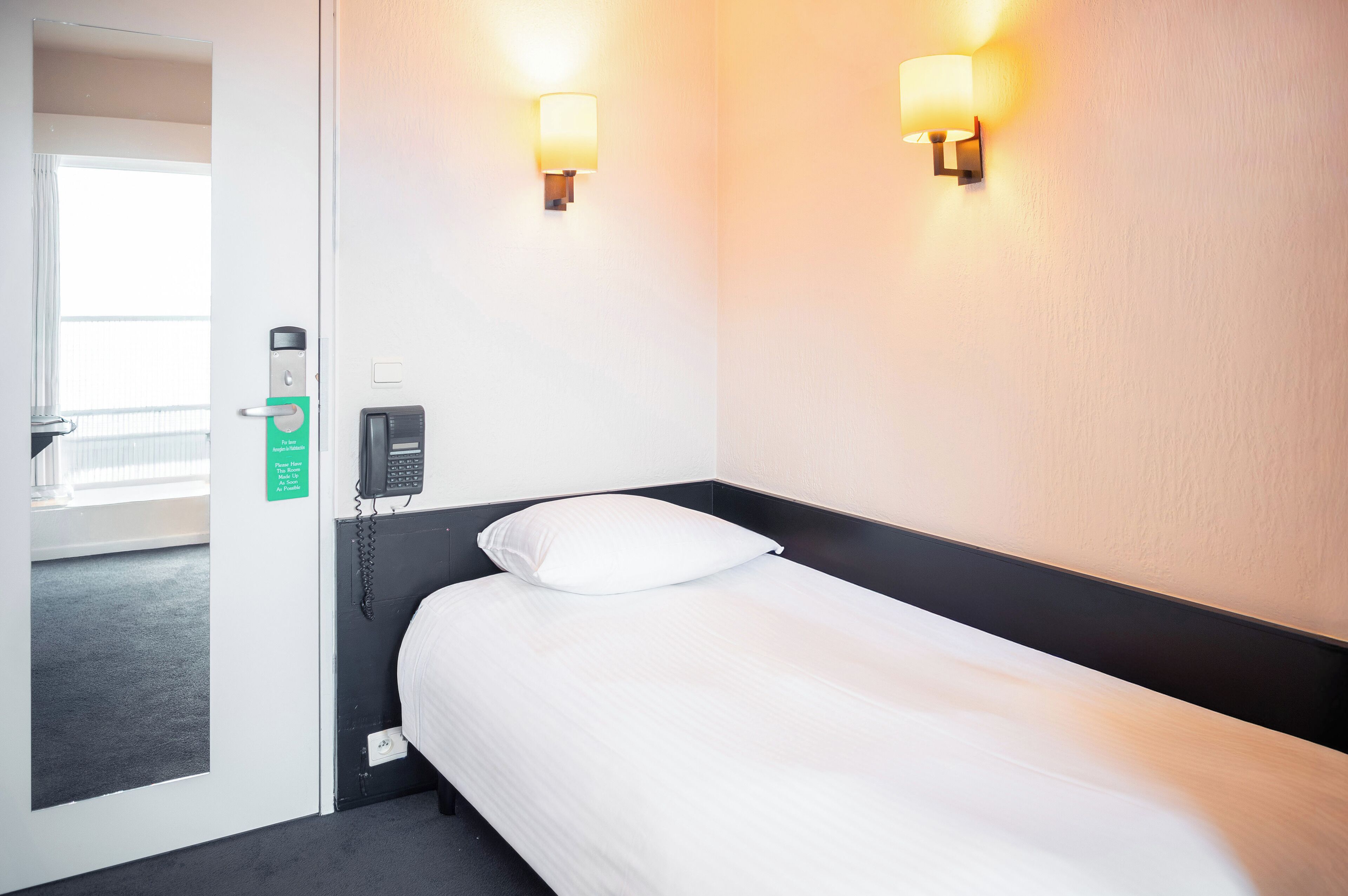 A hotel room with a bed, bedside phone, and two wall-mounted lights.