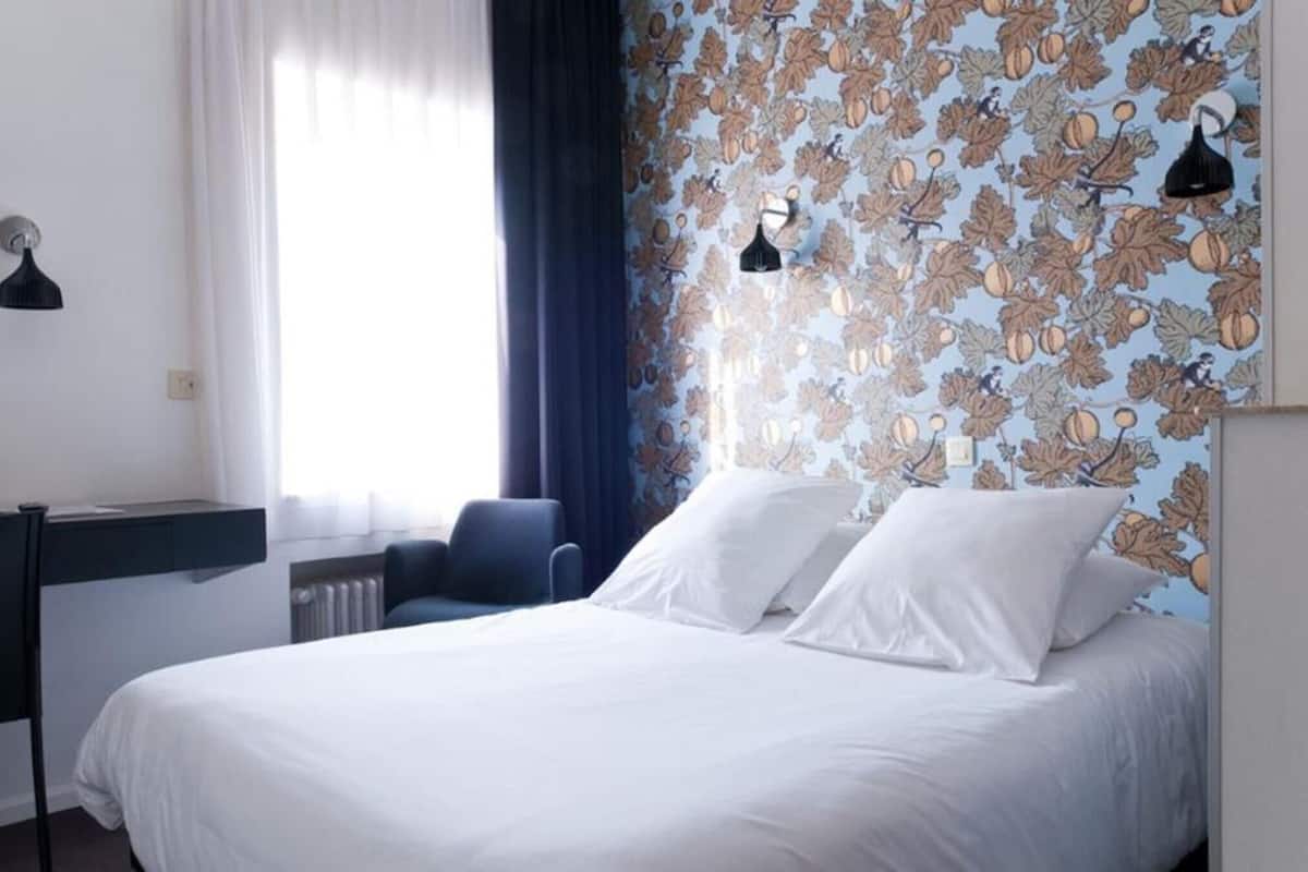 A hotel room with a bed, a desk, and a chair.
