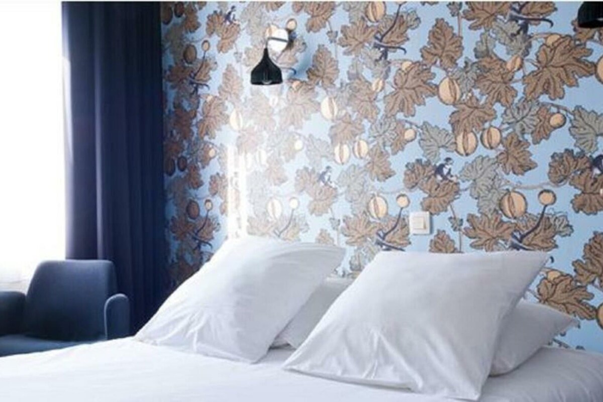 A hotel room with a bed, two pillows, a chair, a lamp, and a window with curtains.