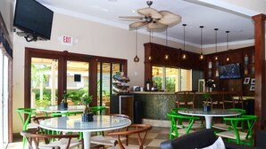 Un ristorante con tavoli rotondi e sedie verdi, una ventola a soffitto e un televisore montato a parete.