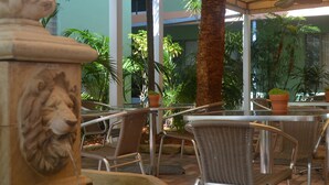 Un'area patio all'aperto con sedie in vimini, una scultura di leone in pietra e piante in vaso.