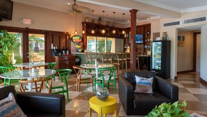 Una hall d'albergo con angolo bar, sedie verdi e bianche, un divano in pelle nera e un tavolino giallo.