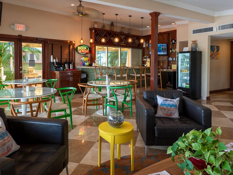 A hotel lobby with a bar area, green and white chairs, a black leather sofa, and a yellow side table.
