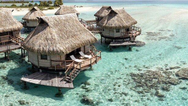 Overwater bungalows met rieten daken, houten loopbruggen en helder turquoise water.