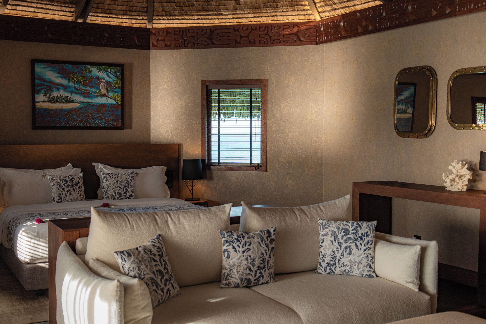 A bedroom with a bed, a sofa, a painting, a window, and a mirror.
