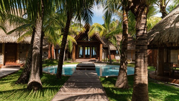 Un resort con piscina, palmeras y edificios de techo de paja.