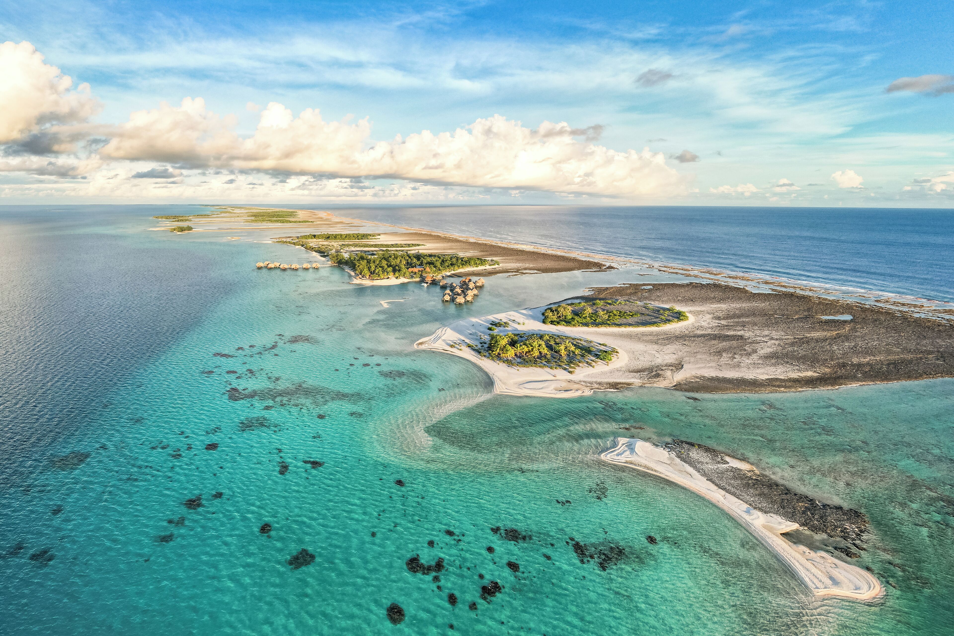 An aerial view of a coastal area with clear turquoise waters, sandy beaches, and small islands with vegetation.