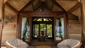 A thatched-roof structure with a wooden frame, two white cushioned chairs, and a wooden table. - Le Tikehau by Pearl Resorts (Tikehau)