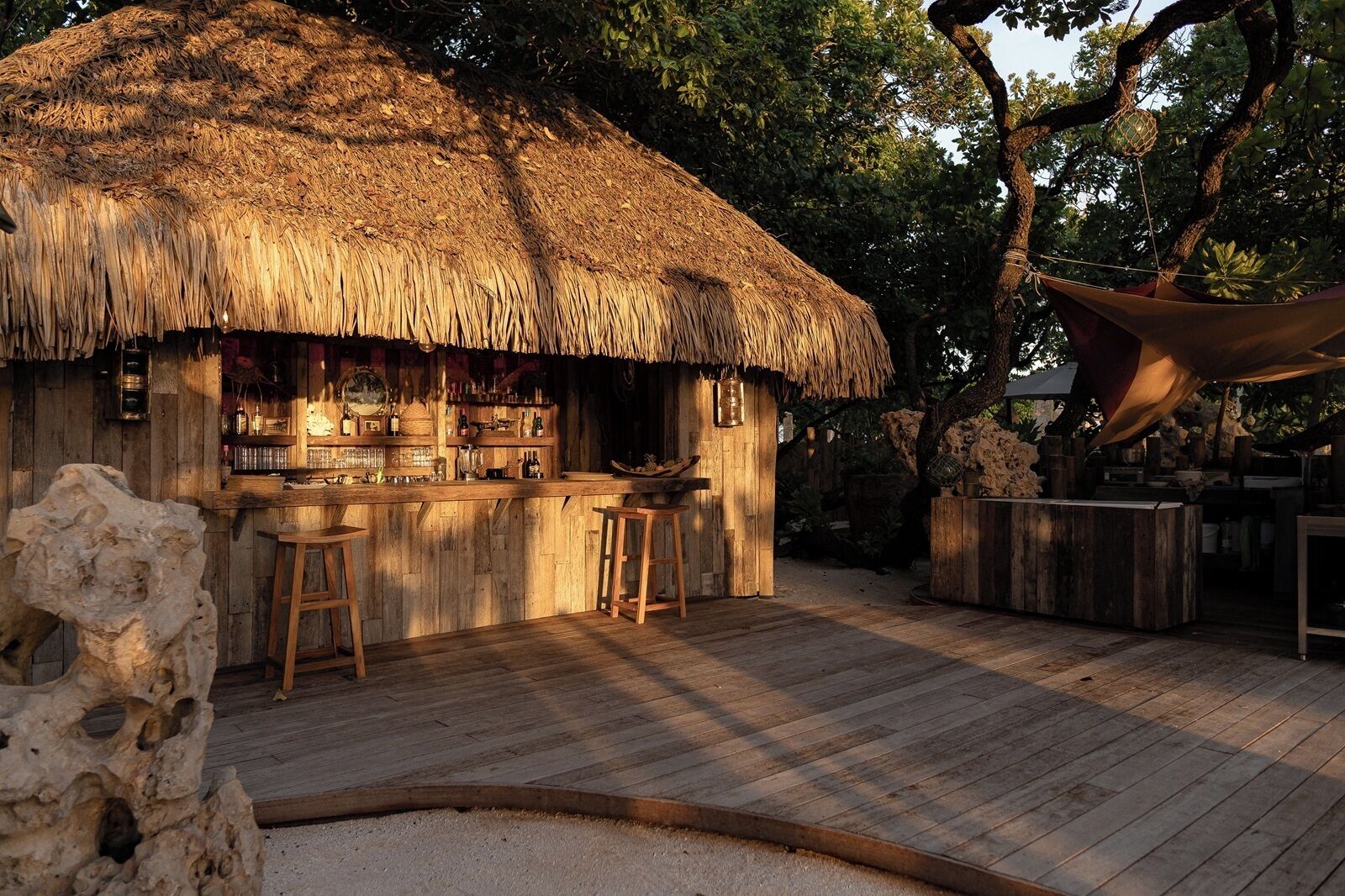 A thatched-roof bar with wooden stools, a wooden counter, and a stone sculpture.