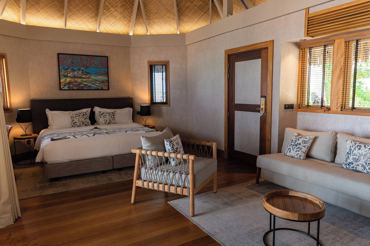 Une chambre à coucher avec un lit, un canapé, une chaise en bois, une table ronde en bois et un tableau accroché au mur.