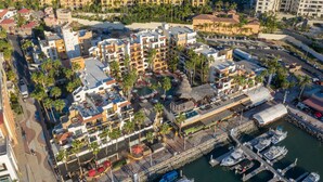 An aerial view of a coastal hotel area with multiple buildings, a marina with boats, and a central plaza with palm trees. - Marina Fiesta Resort & Spa (Cabo San Lucas)