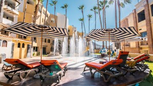A pool area with lounge chairs and umbrellas, surrounded by palm trees and a water fountain. - Marina Fiesta Resort & Spa (Cabo San Lucas)
